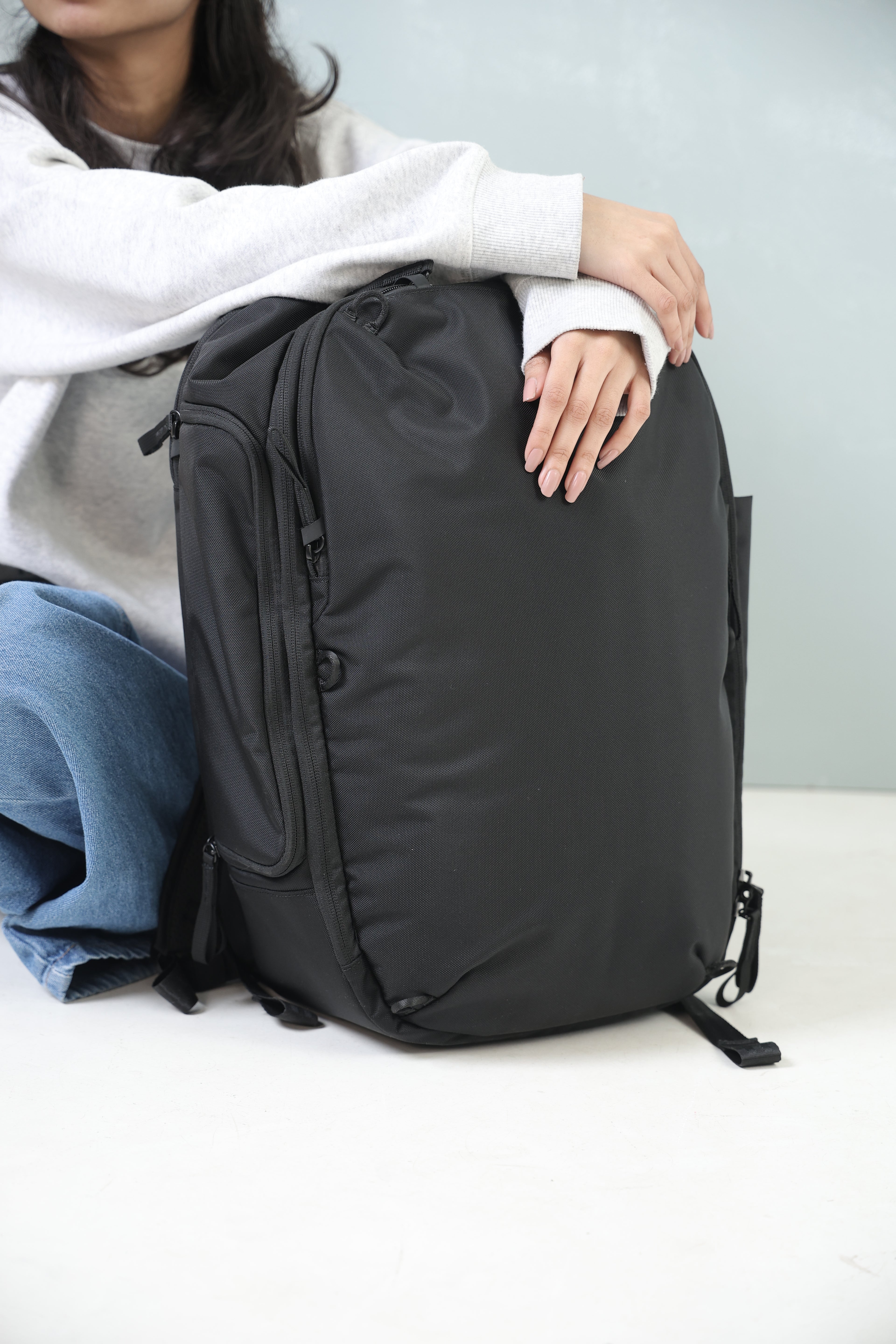 Person holding a black backpack on a light gray surface