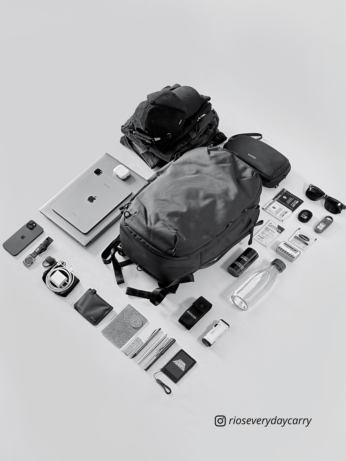 Black and white angled flatlay of Daily Dash with a laptop, clothes, water bottle and everyday accessories