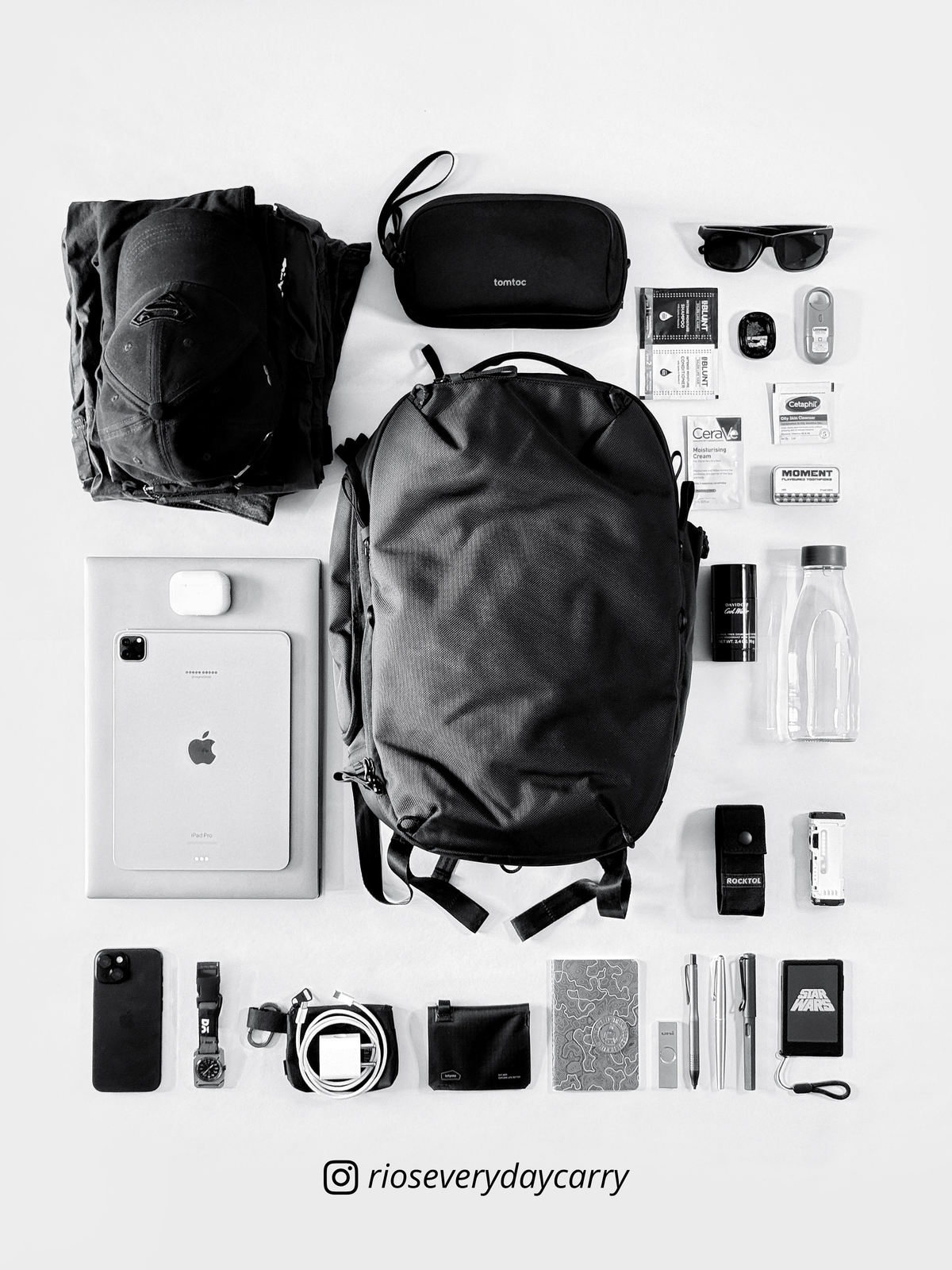 Overhead black and white flatlay of Daily Dash with neatly arranged clothing, technology, bottle and accessories